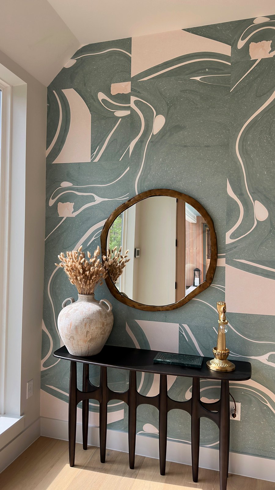 Painterly wallpaper in an entry with a round mirror and console