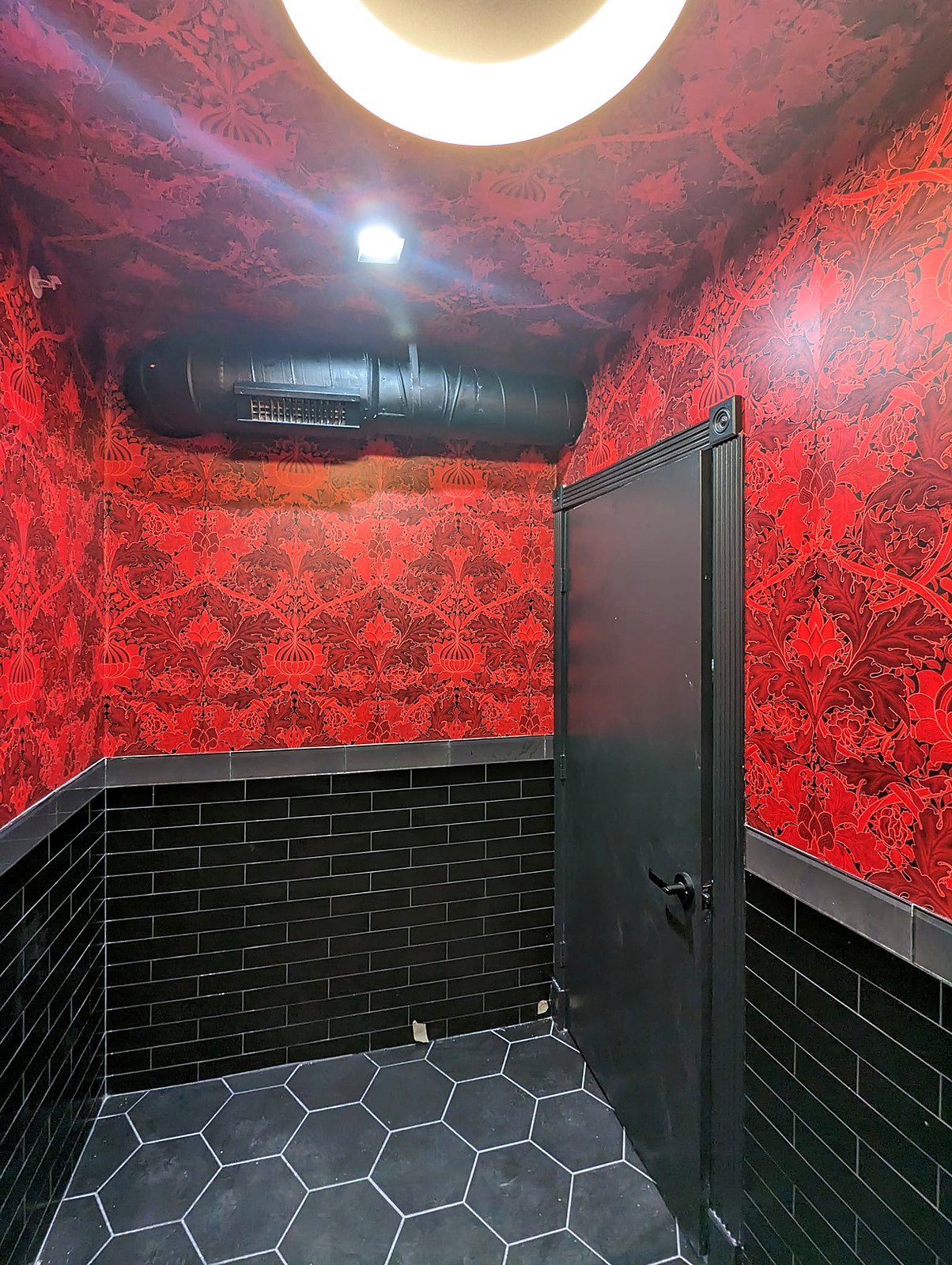 Red patterned wallpaper in a restroom with black tile wainscot