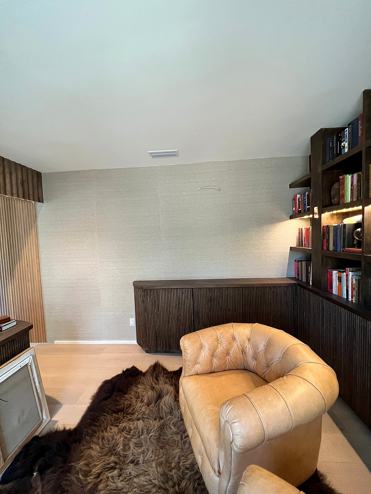 Home office with built-in shelving, a leather chair, and a textured wall